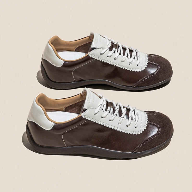 Zapatillas retro de cuero dividido y ante marrón oscuro con ojales dentados y cordones blancos sobre fondo beige