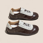 Zapatillas retro de cuero dividido y ante marrón oscuro con ojales dentados y cordones blancos sobre fondo beige