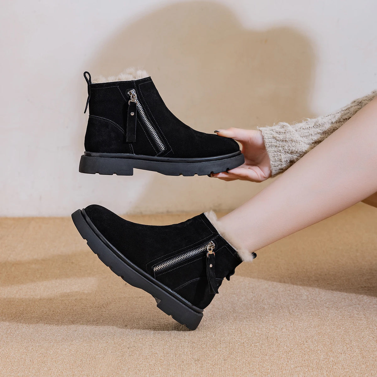 Modin präsentiert schwarze Stiefeletten, hält eine in der Hand und trägt die andere mit Plüschfutter und rauer Plattformsohle