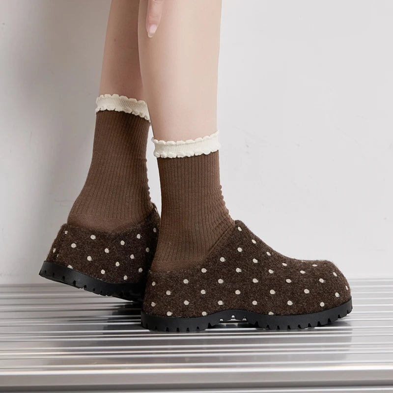 Rückansicht der Füße in braunen Punkt-Slip-On-Clogs stehend auf metallischem Lamellenbänkchen, Fersenkonstruktion betonend