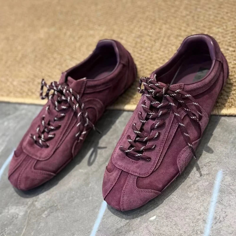 Burgundy retro sneakers with black-and-white speckled laces on grey stone surface