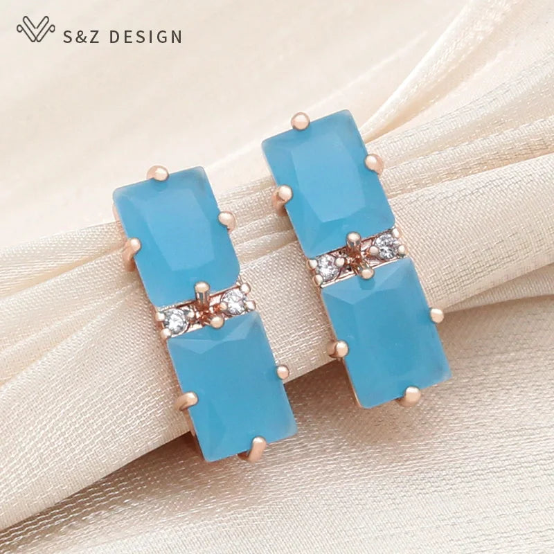 Brincos pendentes retangulares azul-celeste com acabamento polido em tom de rosa e detalhes de cristal sobre tecido pêssego claro