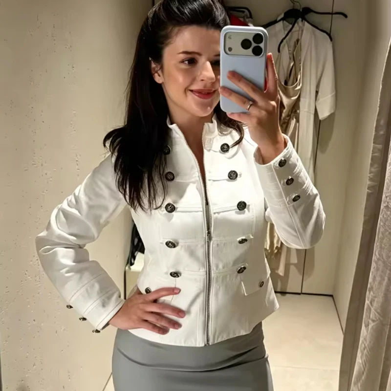 Mulher sorridente com jaqueta branca cremalheira e botões decorativos sobre saia cinza, tira selfie no espelho interior