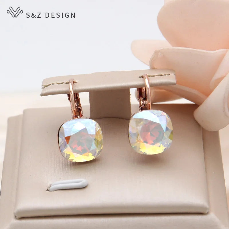 Brincos dourado-rosé S&Z Design com facetas claras AB refletindo tons pastel junto a suporte de joias bege