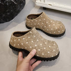 Kamelbraune Punkt-Clogs in der Hand, die weiches Flanellfutter und das rückfreie Slip-On-Design auf grauer Oberfläche zeigen