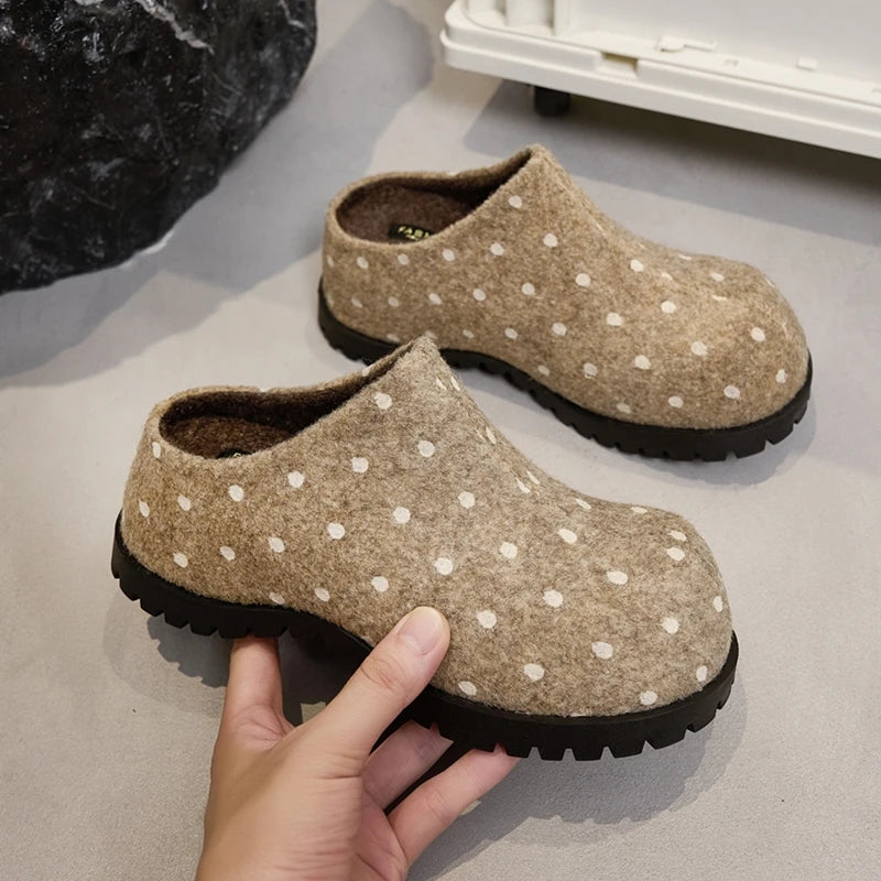 Kamelbraune Punkt-Clogs in der Hand, die weiches Flanellfutter und das rückfreie Slip-On-Design auf grauer Oberfläche zeigen