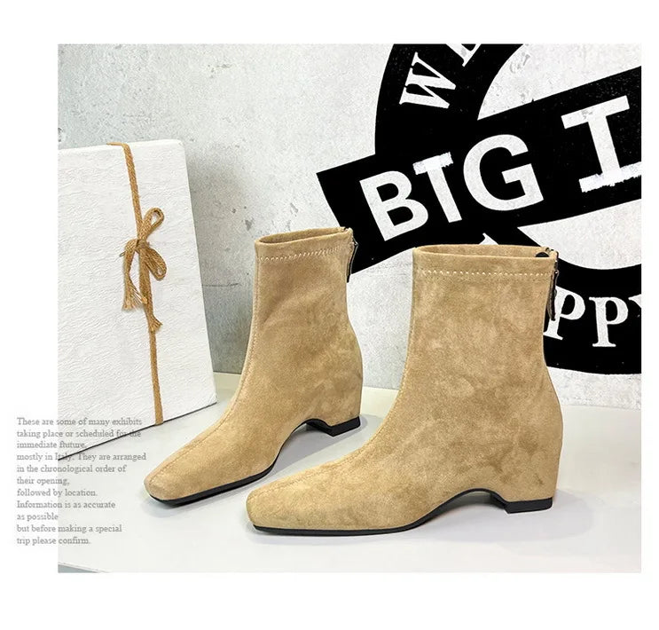 Zwei beige Wildlederschnürsenkel-Stiefel aufrecht stehend, abgerundete Spitze und 5-8cm Blockabsätze neben Geschenkbox.