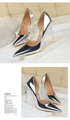 Silberne pointed-toe Pumps mit transparenten Stilettoabsätzen auf weißen Boxen vor beige gestepptem Hintergrund, Vorder- und Seitenansicht