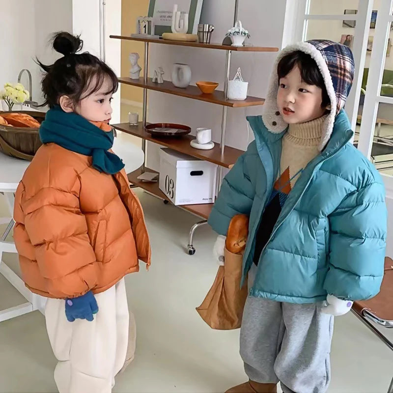 Girl in orange and boy in blue puffer jackets modeling fit with scarves and hats in an indoor setting.