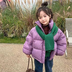 Young girl in lavender short puffer jacket with high stand collar and fuzzy green scarf holding brown handbag.