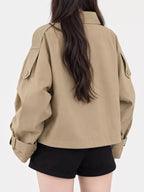Rückansicht des kurzen beigen Jacke mit sauberer Naht, verstellbaren Schnallenbündchen und über schwarzen Shorts