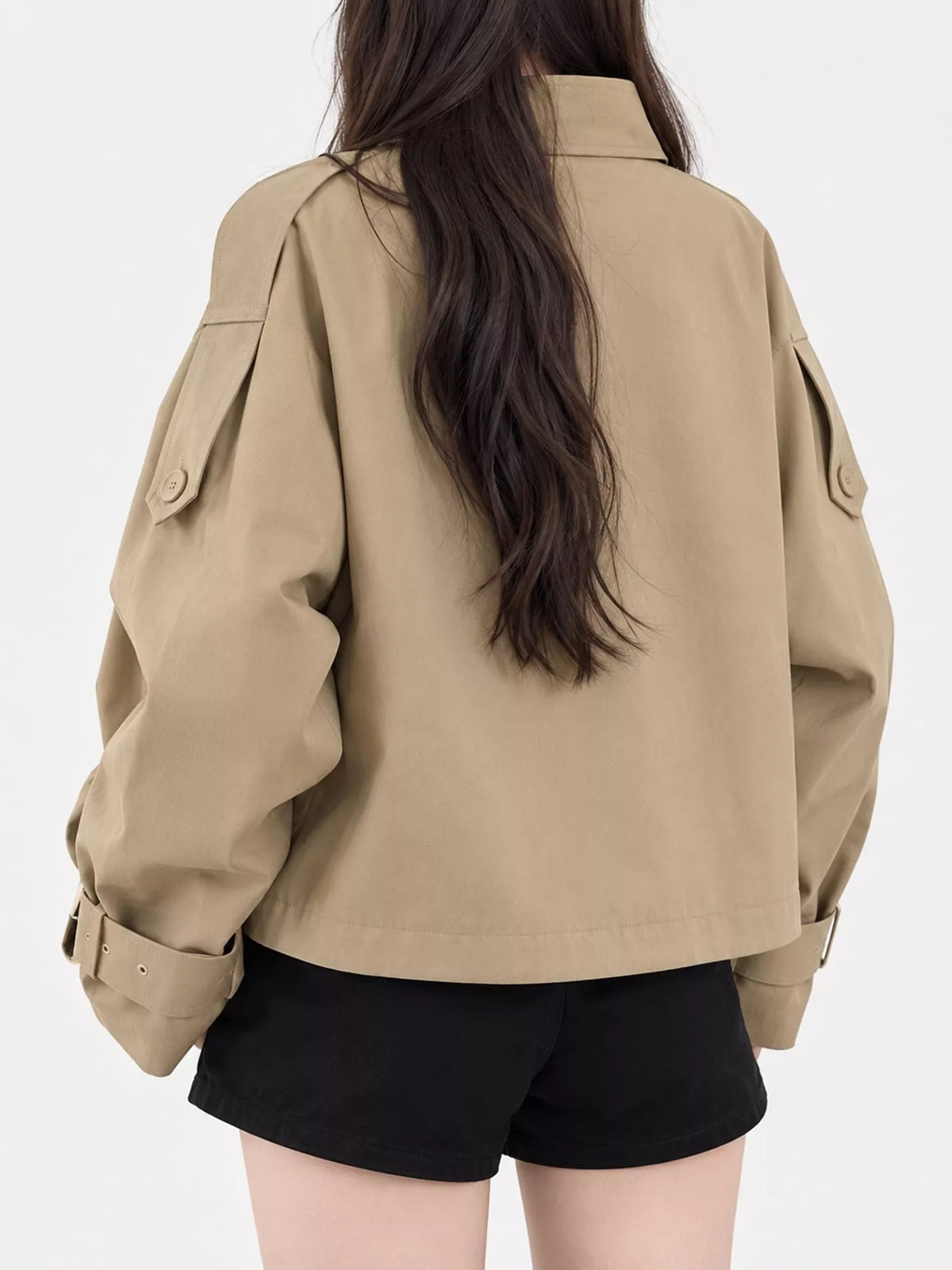 Rückansicht des kurzen beigen Jacke mit sauberer Naht, verstellbaren Schnallenbündchen und über schwarzen Shorts