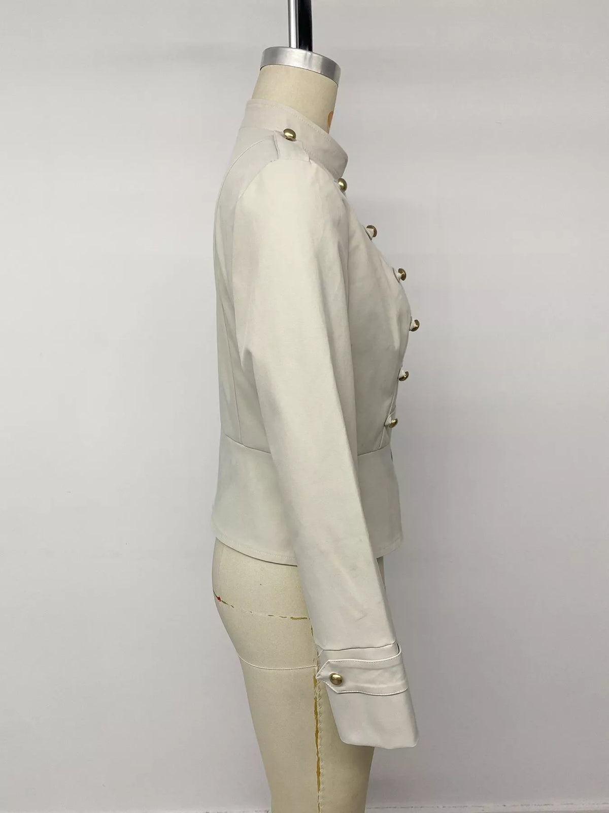 Profil latéral d'une veste cintrée crème mettant en valeur le poignet à bouton unique et la silhouette taille