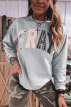 Model in light grey sweatshirt with mixed-media PRAY letters: floral P, pink striped R, plaid A, dark Y. Styled with camo