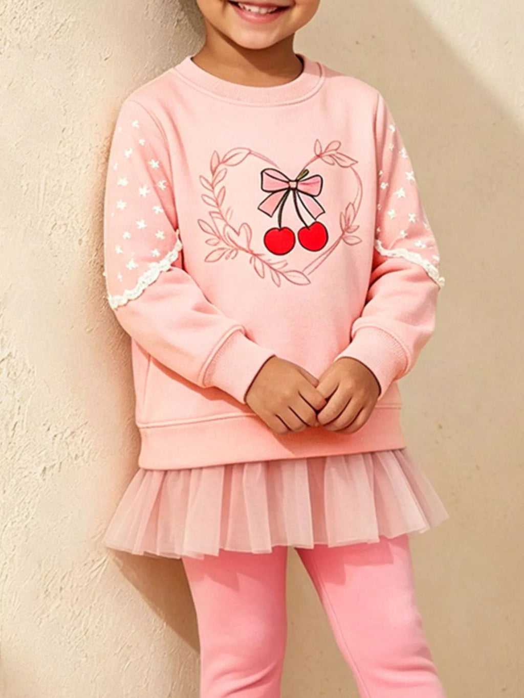 Nahaufnahme: Bestickte rote Kirschen, Schleife und weißer Spitzenbesatz am rosa Sweatshirt