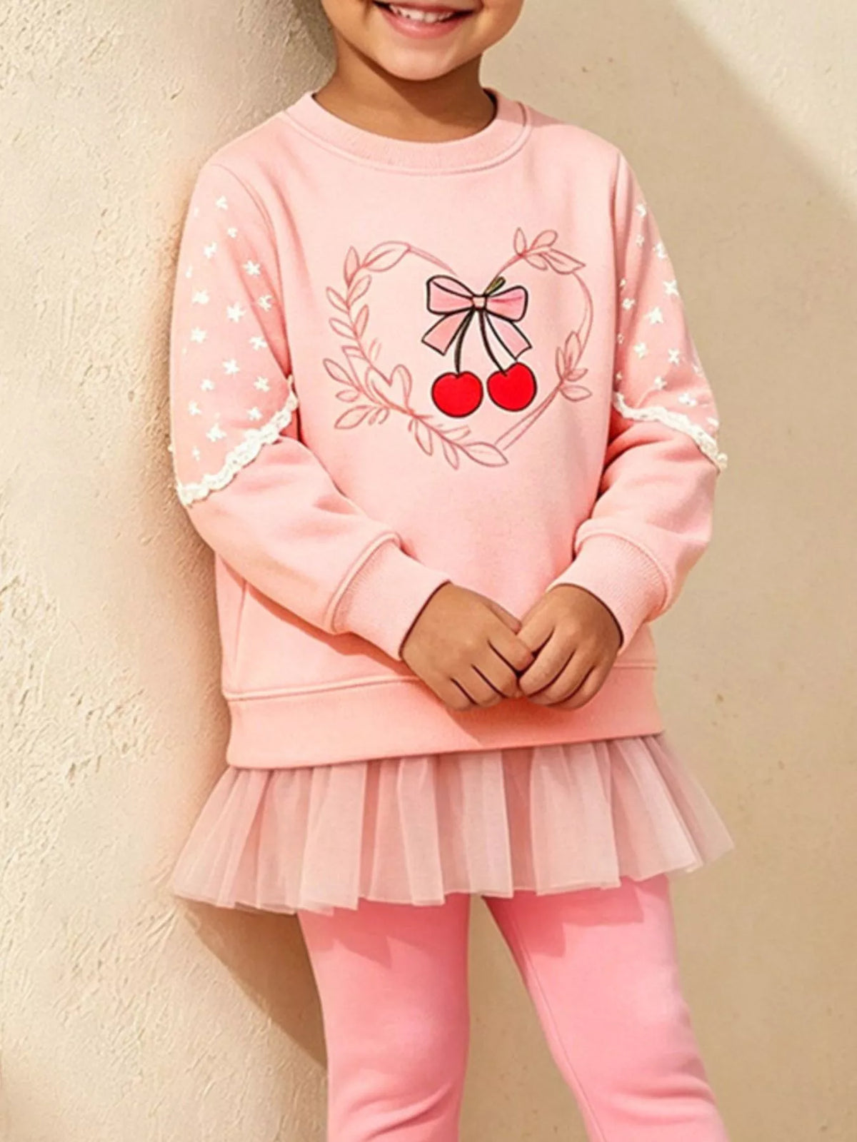 Nahaufnahme: Bestickte rote Kirschen, Schleife und weißer Spitzenbesatz am rosa Sweatshirt