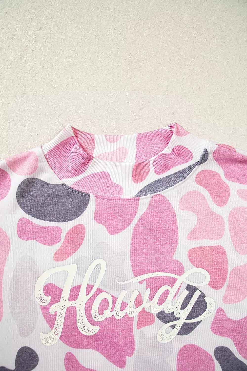 Close-up of ribbed mock neck and white glittery Howdy lettering on soft polyester fabric