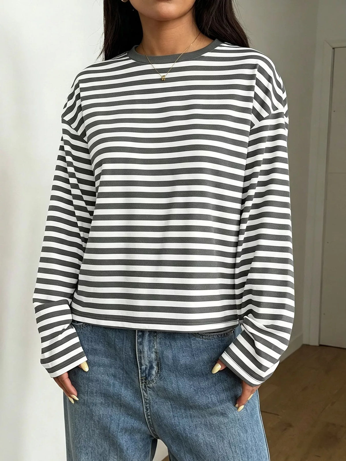 Modella in top maniche lunghe a righe grigie e bianche vicino alle tasche per mostrare la vestibilità ampia e l'alternanza di colori chiari e scuri