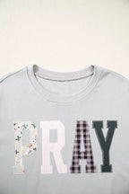 Close-up of front chest displaying PRAY word in large block letters made from floral, pink stripe, black buffalo plaid, and