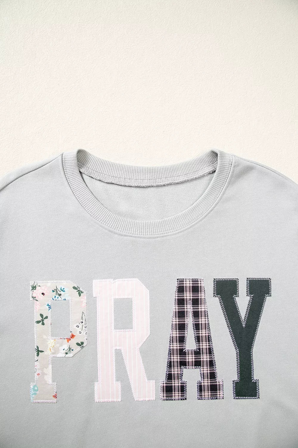 Close-up of front chest displaying PRAY word in large block letters made from floral, pink stripe, black buffalo plaid, and