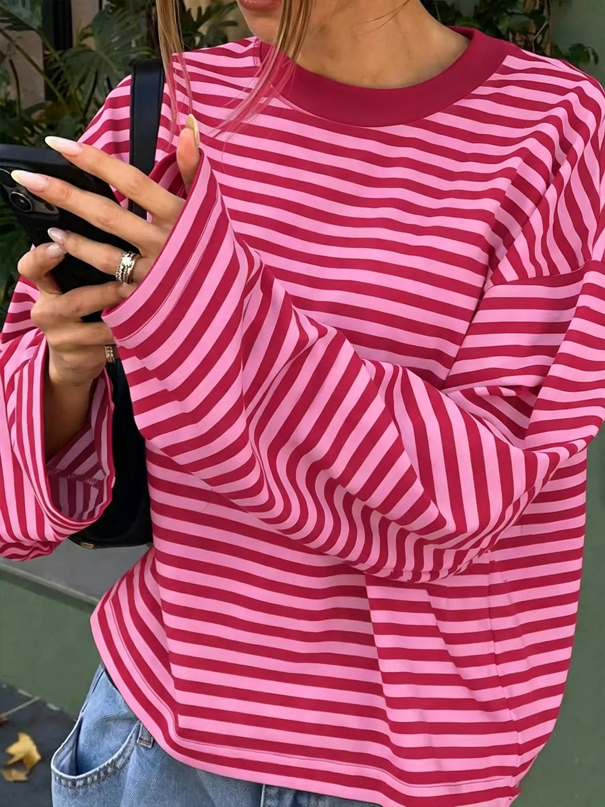 Modella con smartphone nero indossa top a righe rosa e rosso intenso, mettendo in risalto la morbida caduta del tessuto e lo scollo a coste