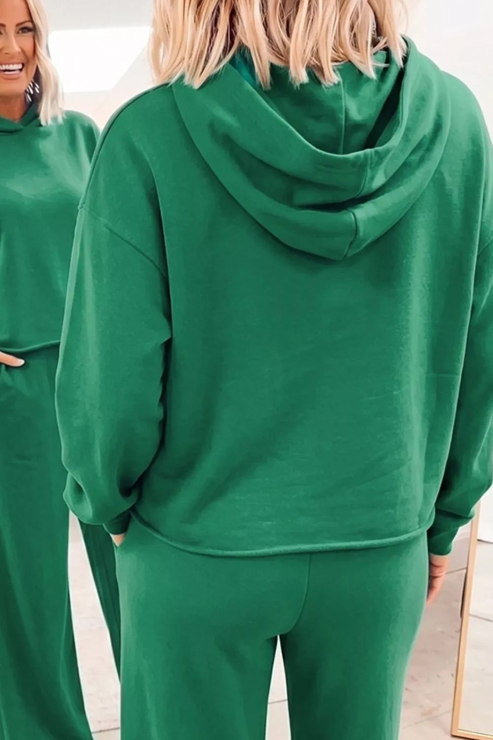 Primer plano del respaldo y capucha de la sudadera verde, mostrando textura de tejido suave y reflejo parcial del espejo.