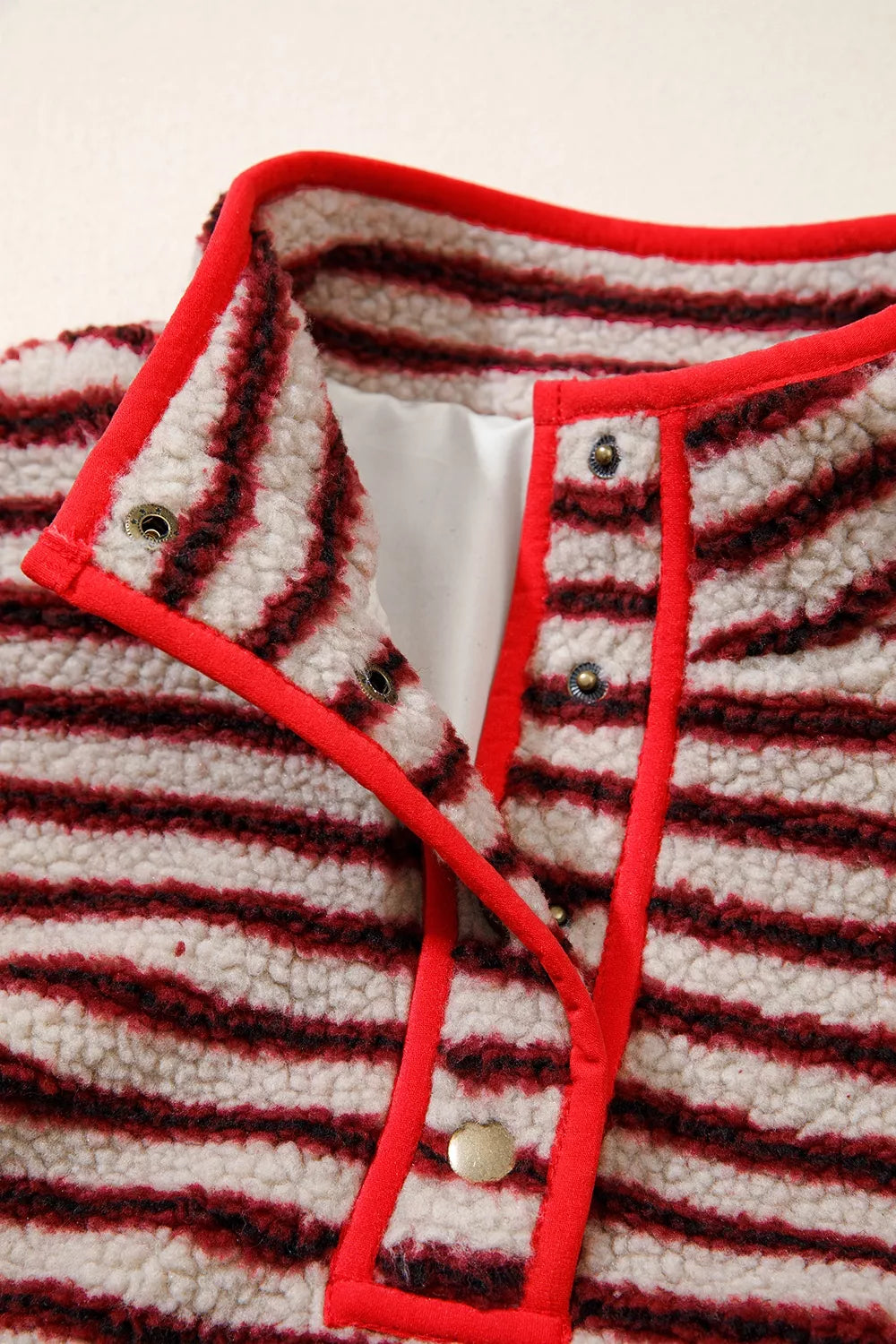 Detalle de cuello abierto: ribete rojo brillante, broches metálicos y forro interior blanco