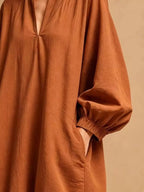 Détail latéral de la robe orange rouille soulignant le poignet élastiqué de la manche ballon et la main dans la poche latérale