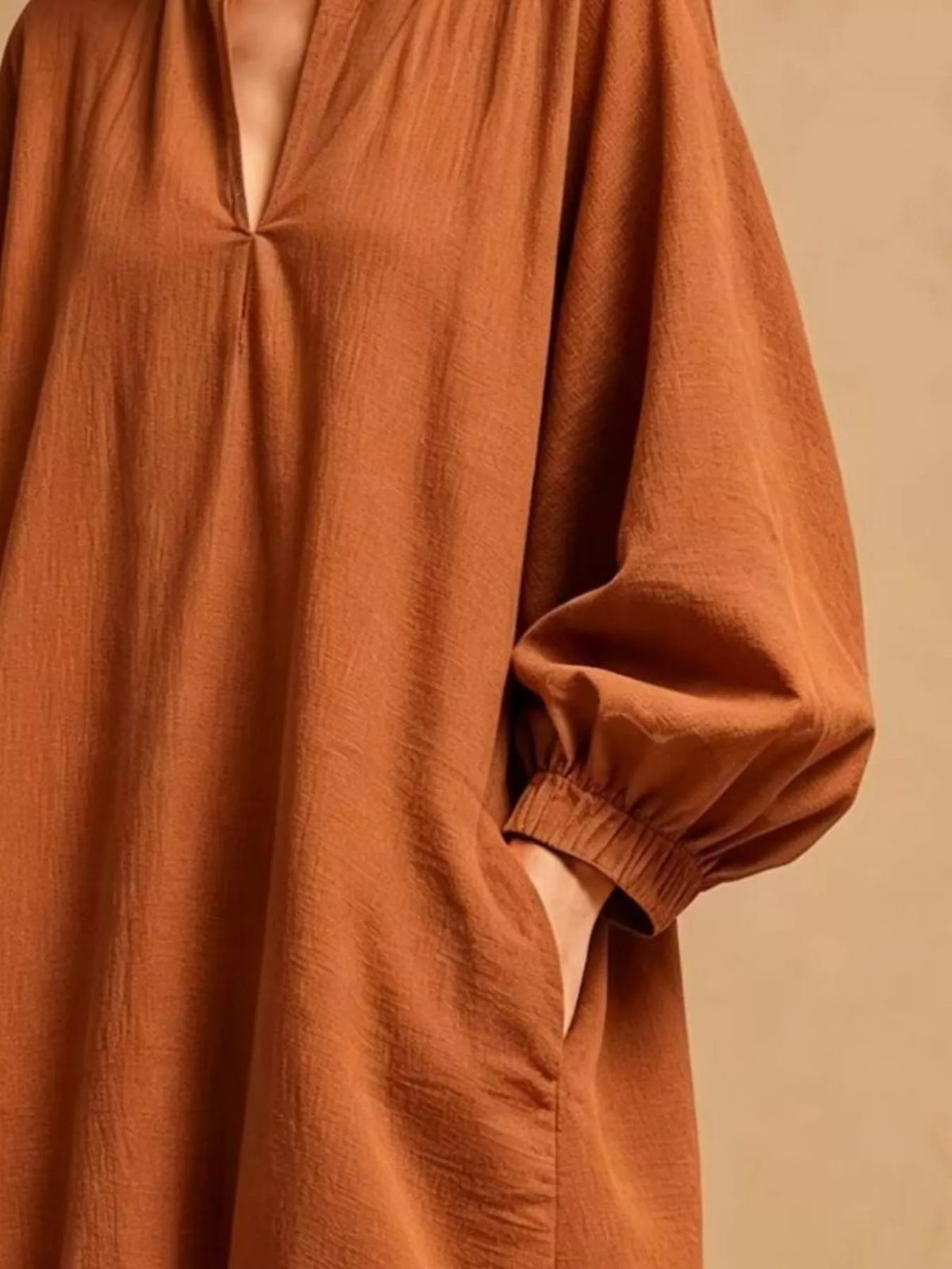 Détail latéral de la robe orange rouille soulignant le poignet élastiqué de la manche ballon et la main dans la poche latérale