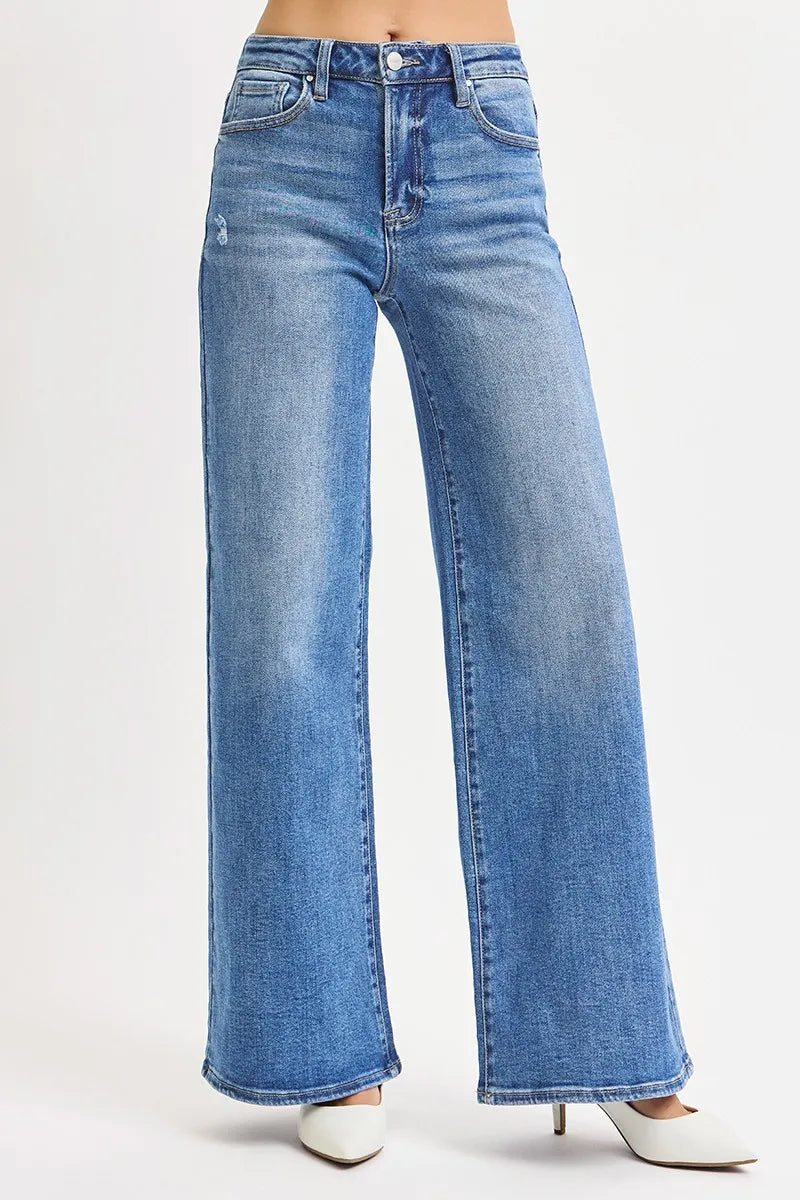 Three-quarter view of wide-leg stretch denim draping over white stilettos, highlighting vertical seams and natural fall