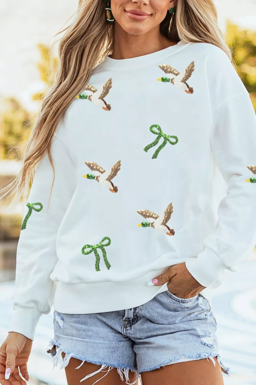 Modèle portant sweat canard pailleté blanc boucles d'oreilles vertes extérieur