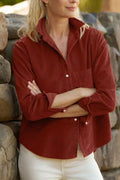 Model in rust-red corduroy shirt with white buttons and chest pocket against stone wall