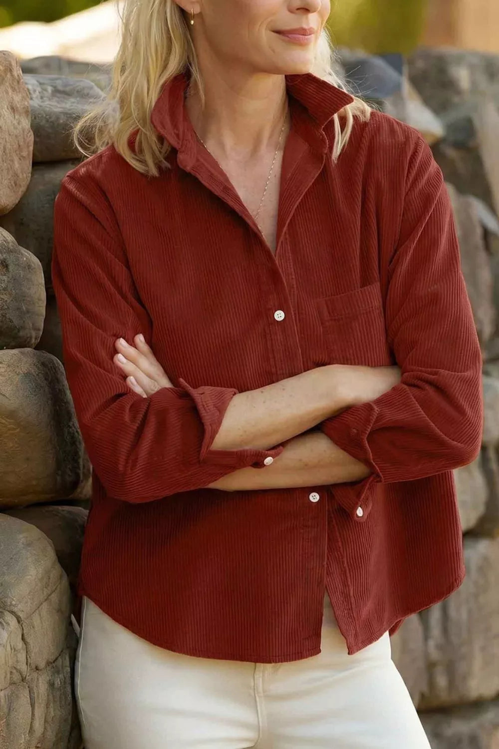 Model in rust-red corduroy shirt with white buttons and chest pocket against stone wall