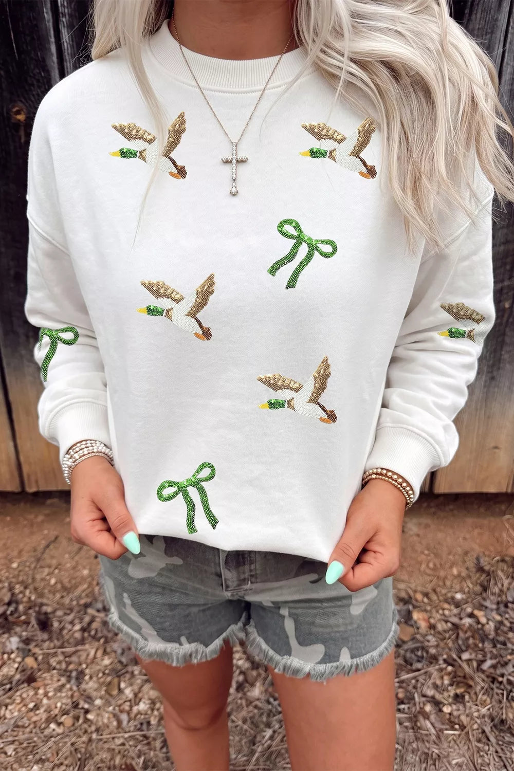 Pull col rond blanc avec canards et nœuds pailletés or/vert sur bois rustique