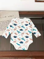 White long-sleeve bodysuit with colorful multi-dinosaur print pattern laid flat on dark wooden surface