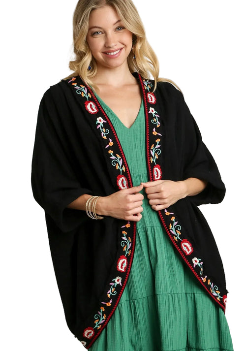 Black open front kimono with vibrant red, white, and teal floral embroidery along the neckline over a green dress