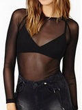 Model in black sheer mesh long sleeve top with high neck over black bralette and denim shorts