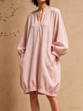 Modèle en mini-robe rose poudré à manches ballon avec les mains dans les poches latérales sur fond beige