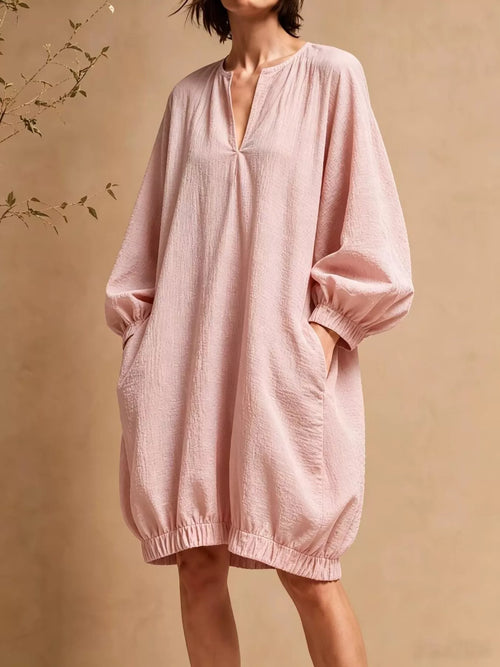 Model in dusty pink balloon sleeve mini dress with hands in side pockets against beige background
