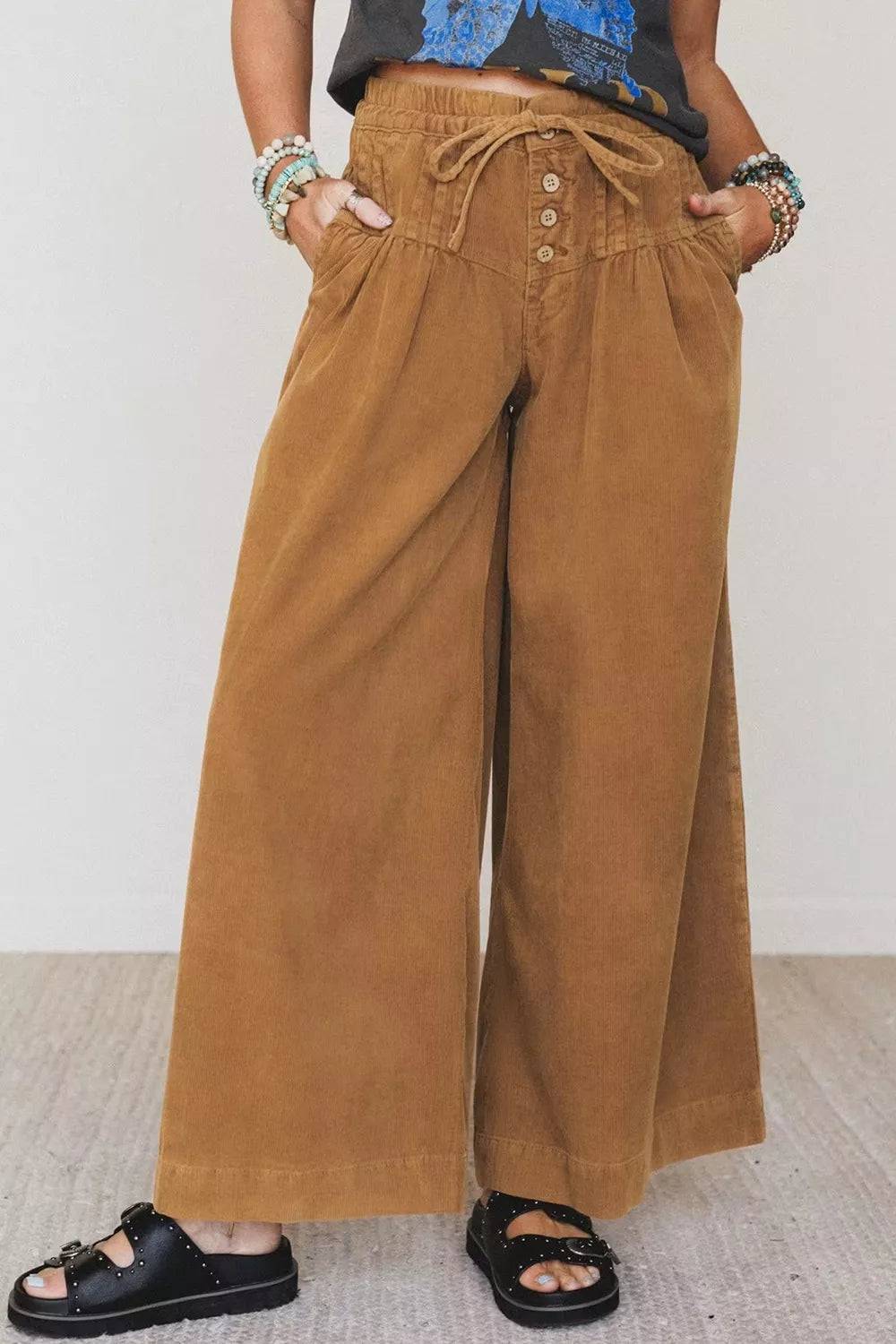 Modelo con pantalones de pana camel de pierna ancha, cintura elástica, botones de madera y manos en bolsillos laterales