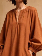 Gros plan de la robe orange rouille montrant la texture froissée et le col rond avec grande boutonnière en V