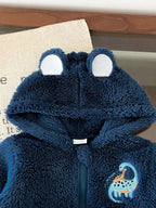Close-up of navy blue soft plush hoodie showing textured fabric, upright bear ears, and embroidered light blue dinosaur