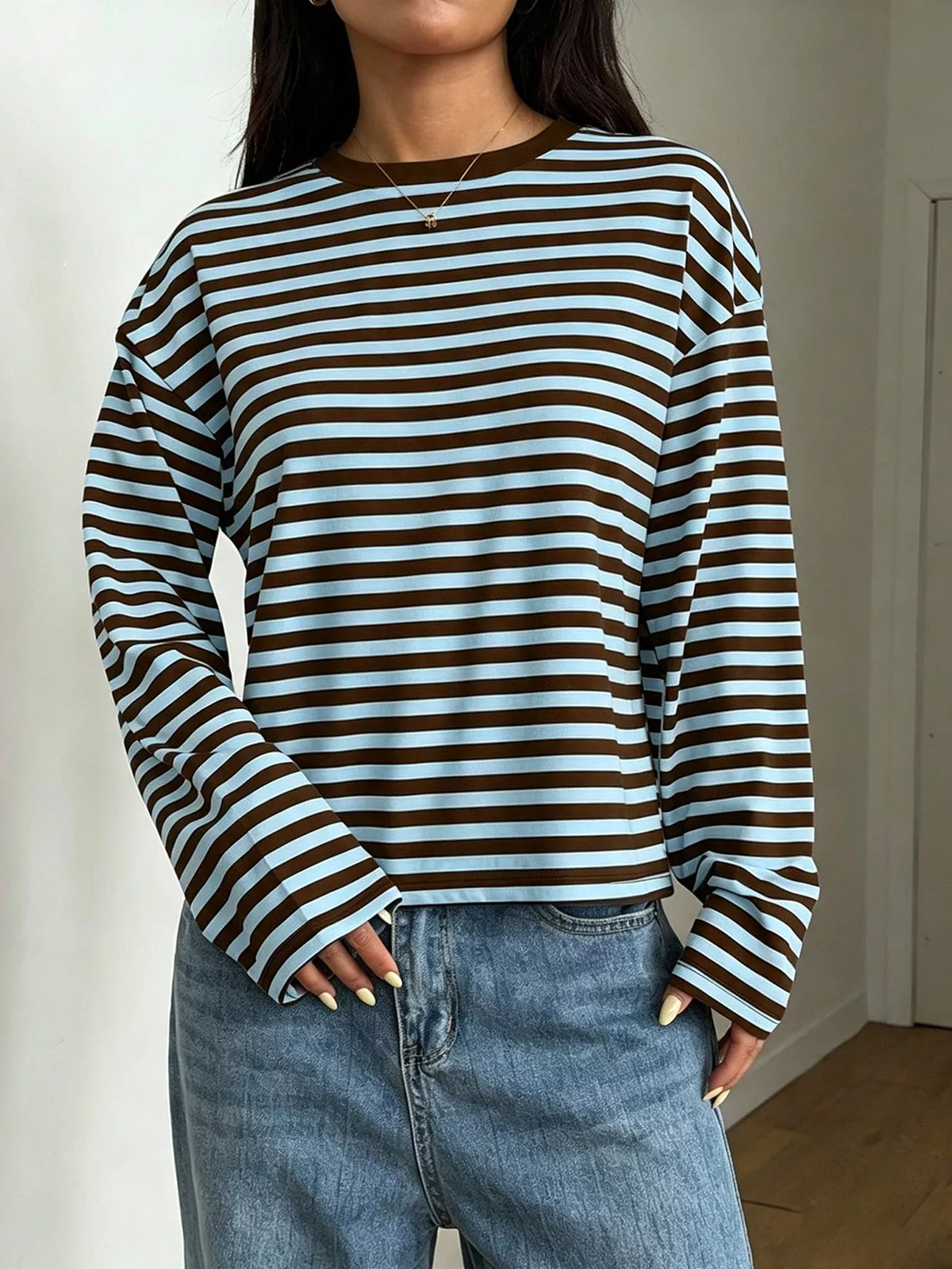 Front view of model in brown and light blue striped long sleeve tee paired with blue denim jeans against plain white
