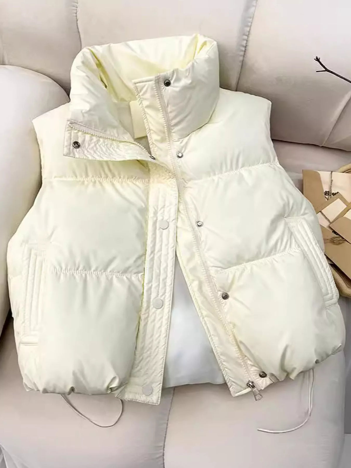 Cream puffer jacket draped on beige sofa in lifestyle setting with packaging