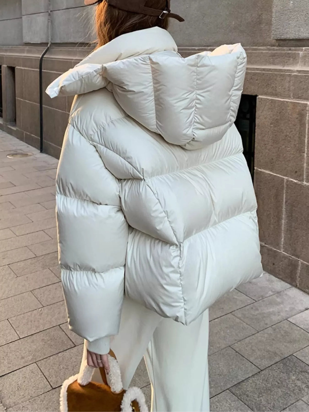 Rear lifestyle shot of model in oversized cream quilted puffer jacket walking on paved street holding bag
