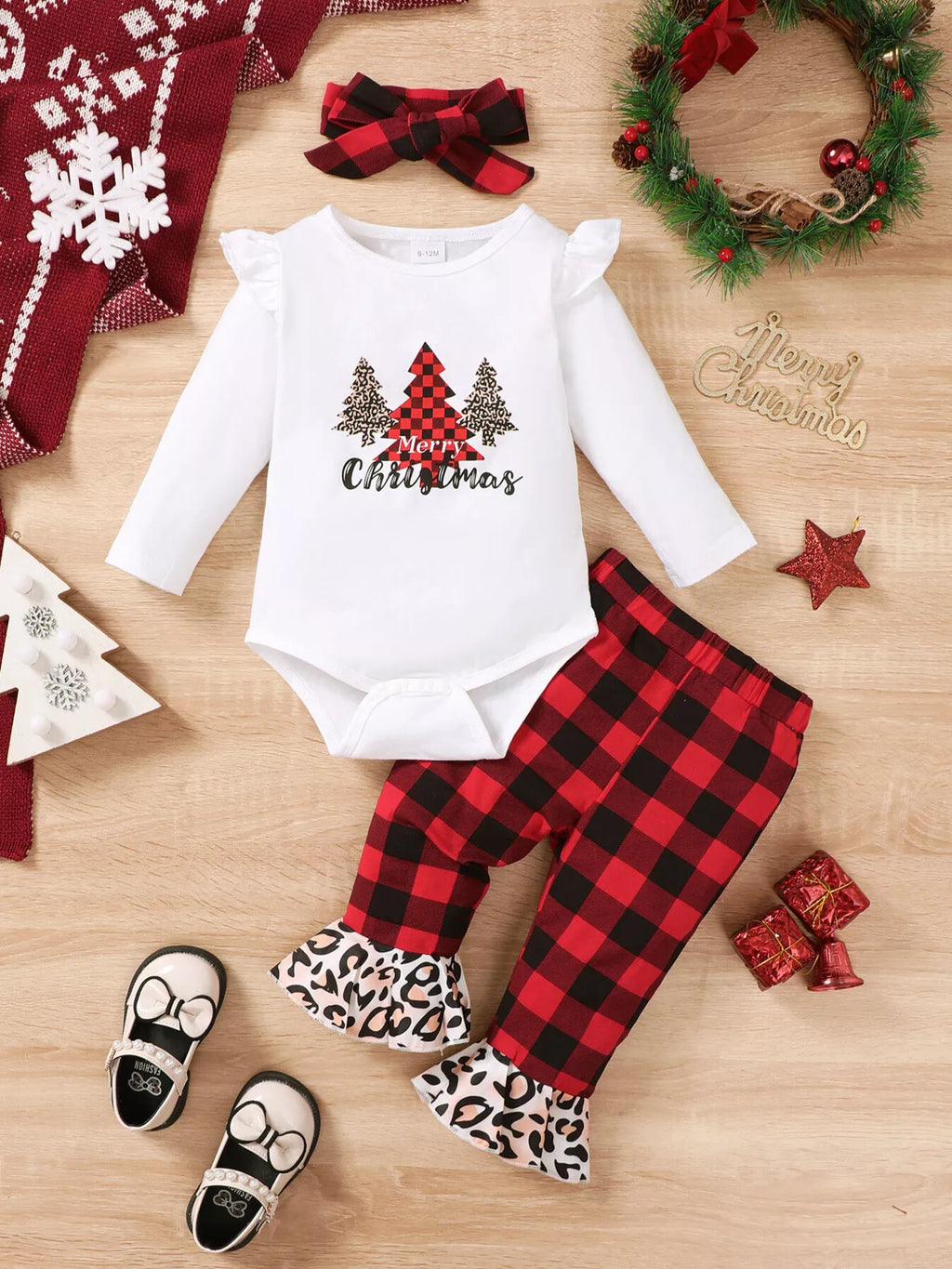 Disposición plana del conjunto navideño para bebé con body de árbol, pantalones a cuadros, diadema, zapatos y accesorios festivos