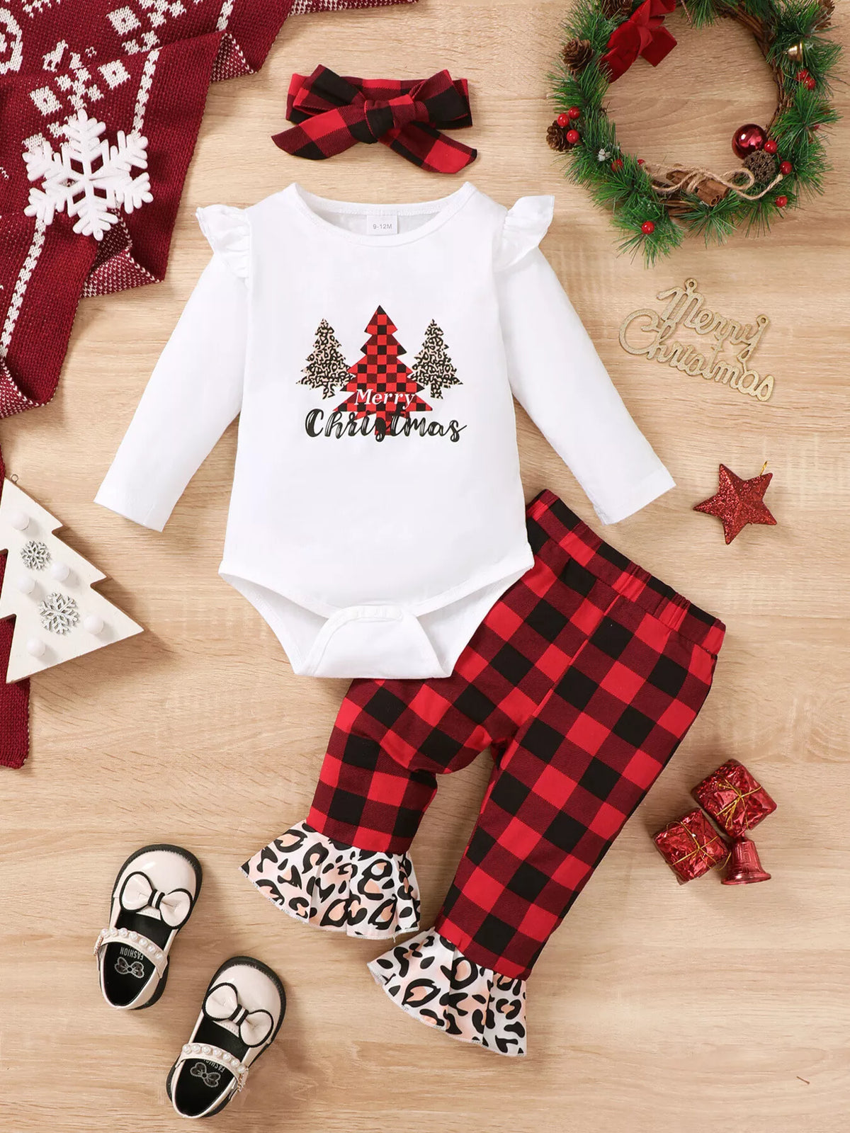 Disposición plana del conjunto navideño para bebé con body de árbol, pantalones a cuadros, diadema, zapatos y accesorios festivos