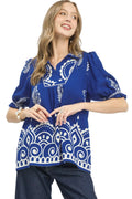 Model in azure blue paisley puff sleeve top with split V-neck and ruffled sleeves against white background