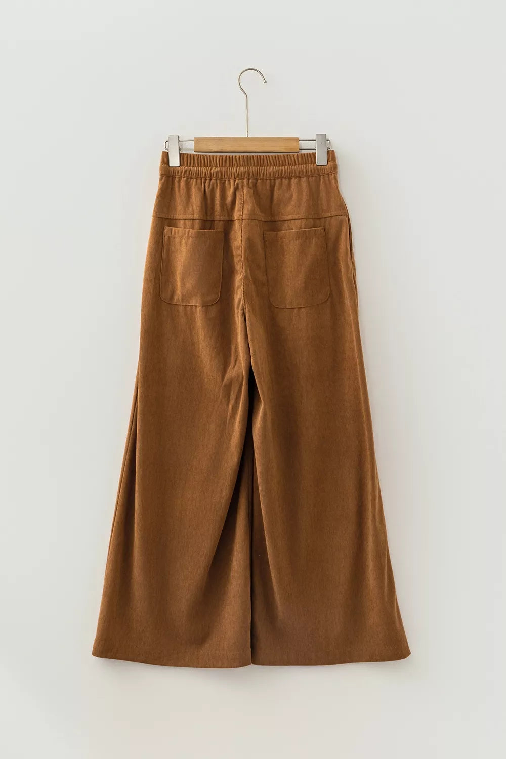 Plano trasero de pantalones de pana camel colgados, destacando la colocación de los bolsillos traseros rectangulares