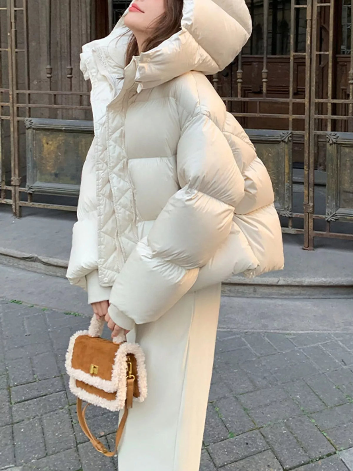 Side profile of model holding brown shearling bag, displaying thick insulation and oversized hood details